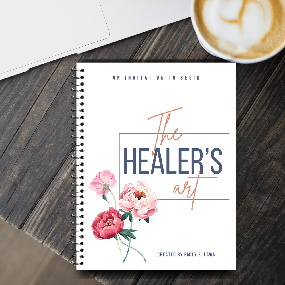 The Healer’s Art Workbook placed on a dark wooden desk beside a latte and a laptop, suggesting a cozy, mindful morning or creative workspace.